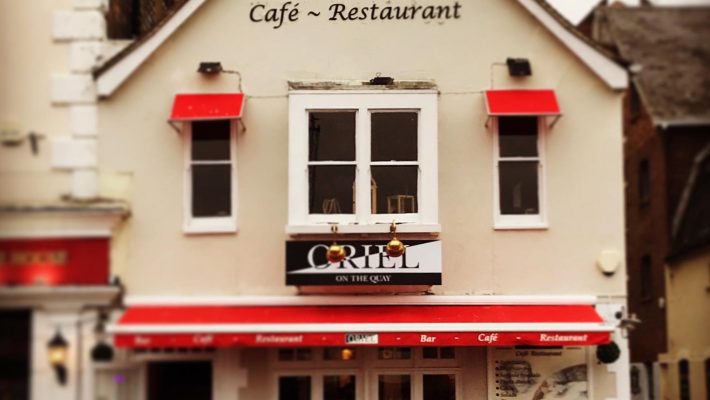 Oriel Café and Restaurant exterior with red awnings and outdoor seating, inviting atmosphere on the quay