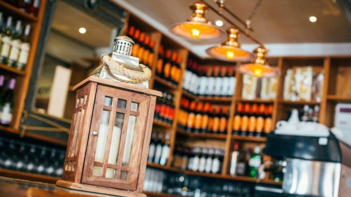 Rustic wooden lantern on a bar counter with wine bottles and warm lighting in the background of a cosy pub interior