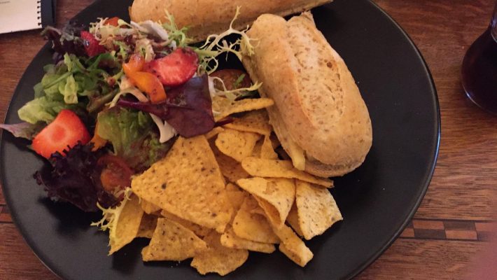 Sandwiches with crunchy tortilla chips and fresh salad on a black plate, served on a wooden table