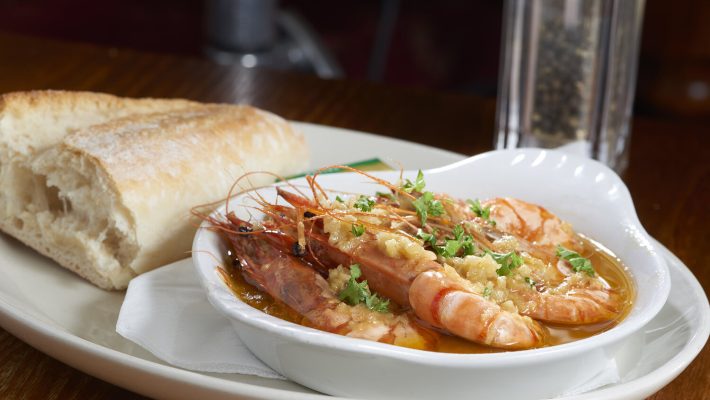 Gambas al ajillo with crusty bread on a white plate, garnished with parsley, served at a restaurant table