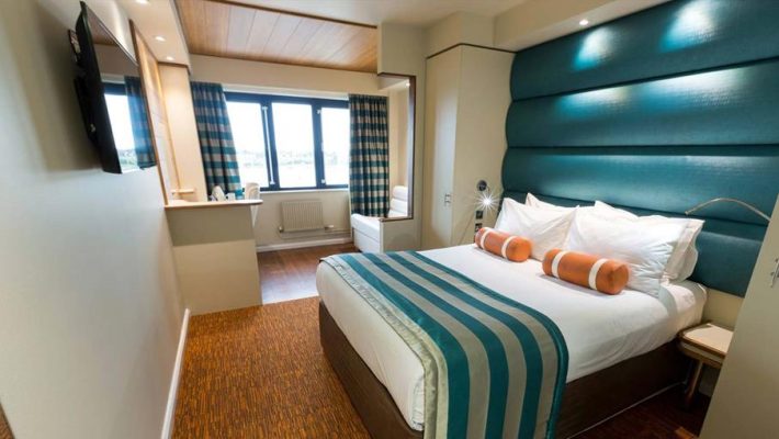 Modern hotel room with cosy double bed, teal accents, and large window for natural light