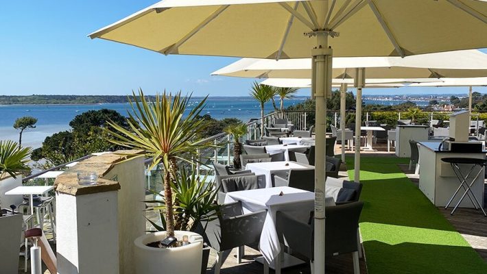 Outdoor seaside restaurant terrace with parasols, white tablecloths, and stunning ocean view on a sunny day