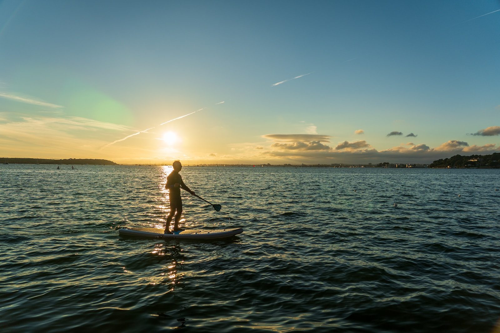 Person paddleboarding on calm sea during sunset with a scenic horizon